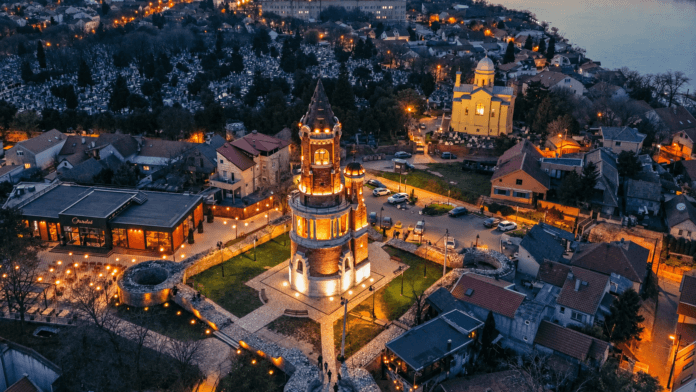 Pogled iz vazduha na osvetljenu Gardošku kulu i krovove Zemuna u sumrak, sa Dunavom u pozadini.